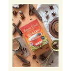 A top-down view of Royal Karak Chai sweetened instant tea box surrounded by whole spices including star anise, cinnamon sticks, cloves, and nutmeg.