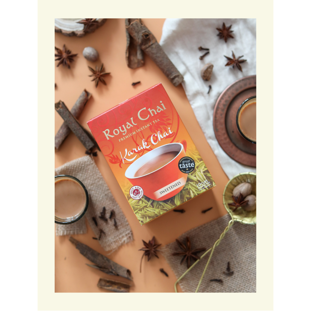A top-down view of Royal Karak Chai sweetened instant tea box surrounded by whole spices including star anise, cinnamon sticks, cloves, and nutmeg.