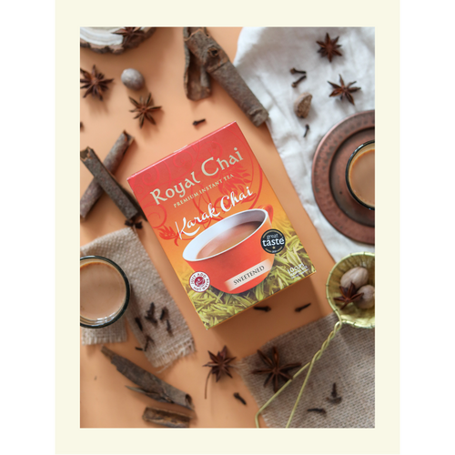 A top-down view of Royal Karak Chai sweetened instant tea box surrounded by whole spices including star anise, cinnamon sticks, cloves, and nutmeg.